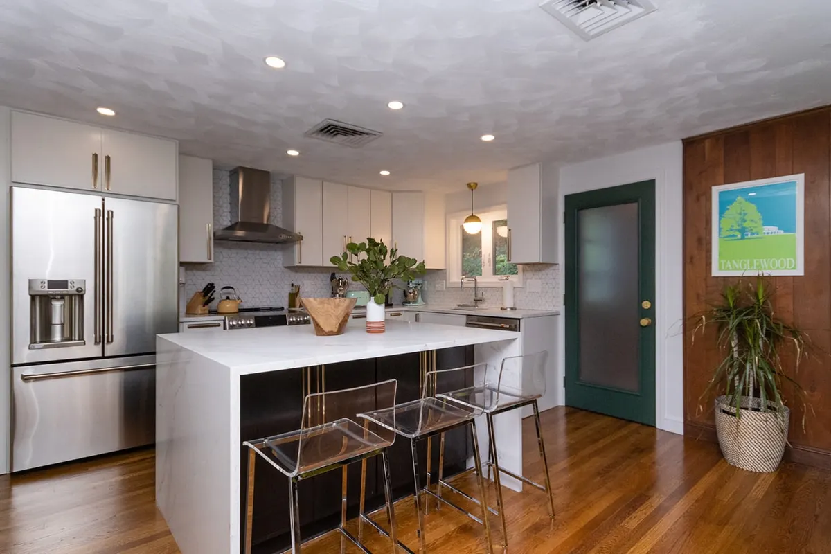A completed Bay State kitchen remodel on Wallis Rd, Chestnut Hill, light gray shaker cabinets, a marble-look waterfall island, hexagon-tile backsplash, and a stainless refrigerator